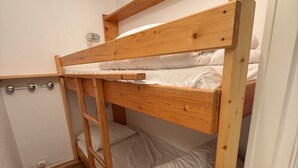 Una cama litera con escalera, cabecera de madera y ropa de cama blanca.