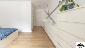 A narrow hallway with a wooden floor, a white wall with a geometric design, and a plant on a shelf. - Apartment Brlog (Zgornje Gorje)