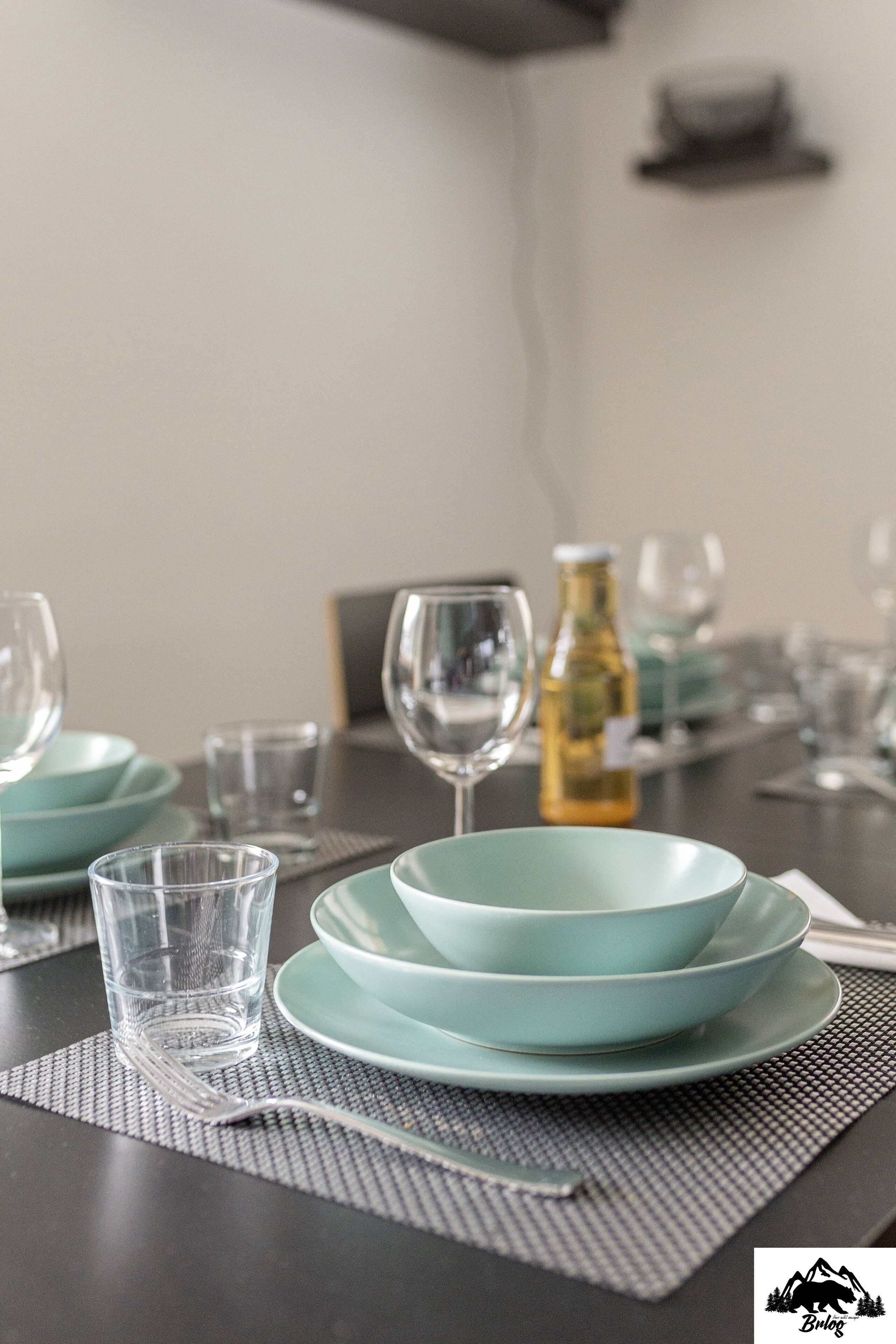 A dining table set with teal plates, glasses, and a bottle.