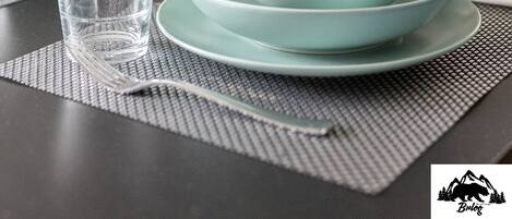 A dining table set with teal plates, glasses, and a bottle.