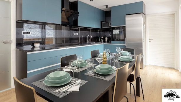 A modern kitchen with blue cabinets, a black countertop, and a dining area set for six. - Apartment Brlog (Zgornje Gorje)