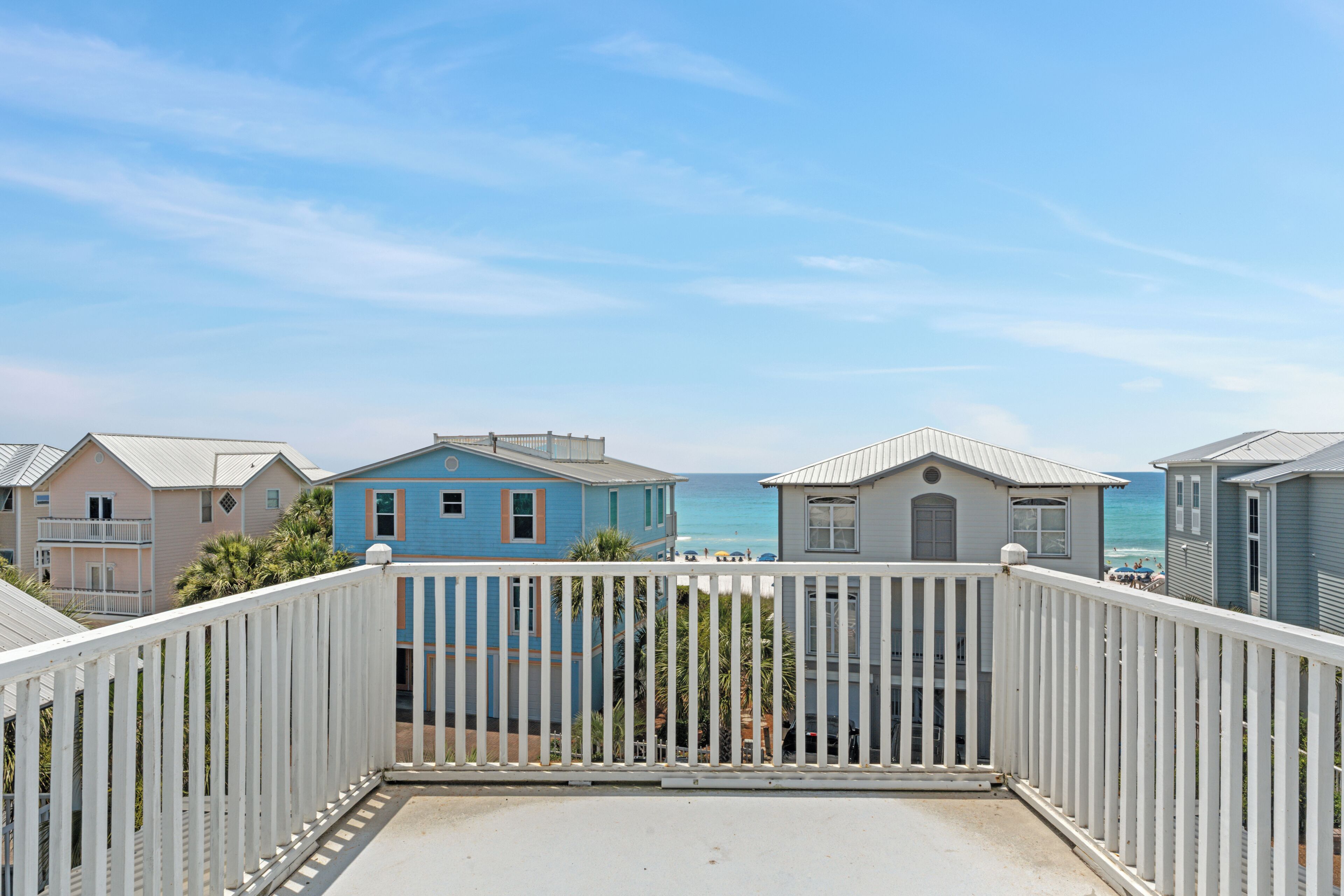 A balcony with a view of the ocean, surrounded by houses with a white fence.