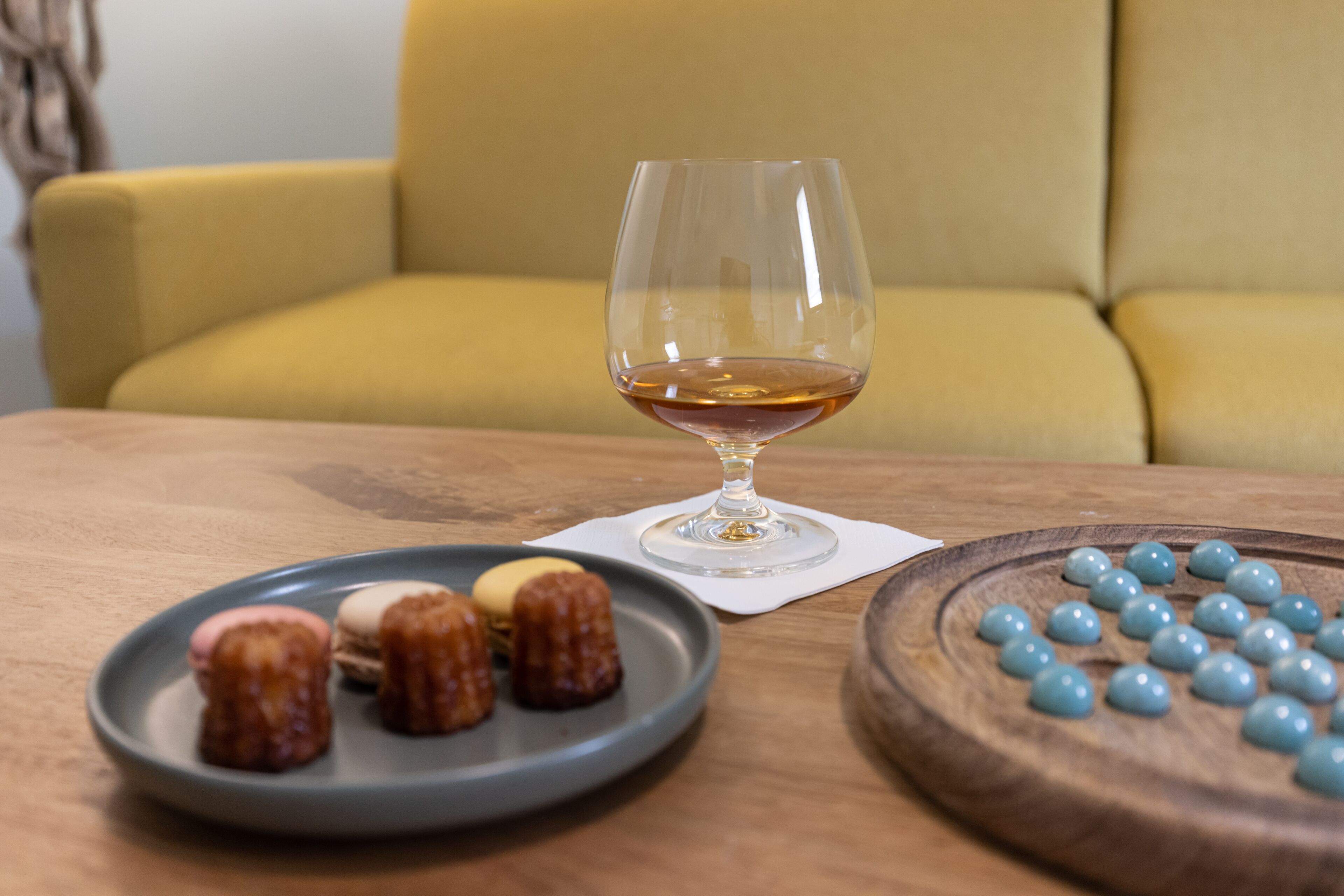 A table with a glass of amber liquid, a plate with small pastries, and a wooden board with round objects.