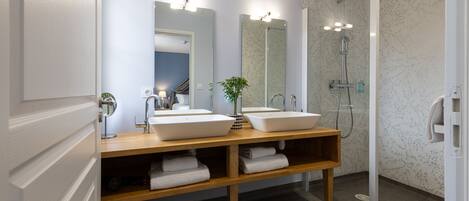 A modern bathroom with two sinks, a mirror, a shower, and a wooden vanity.
