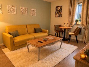 A living room with a sofa, coffee table, and chairs, a small round table with a bottle and candle, and a window with curtains. - Hôtel des Augustins - Boutique Hôtel - Restaurant Gastronomique (Saint-Cyprien)
