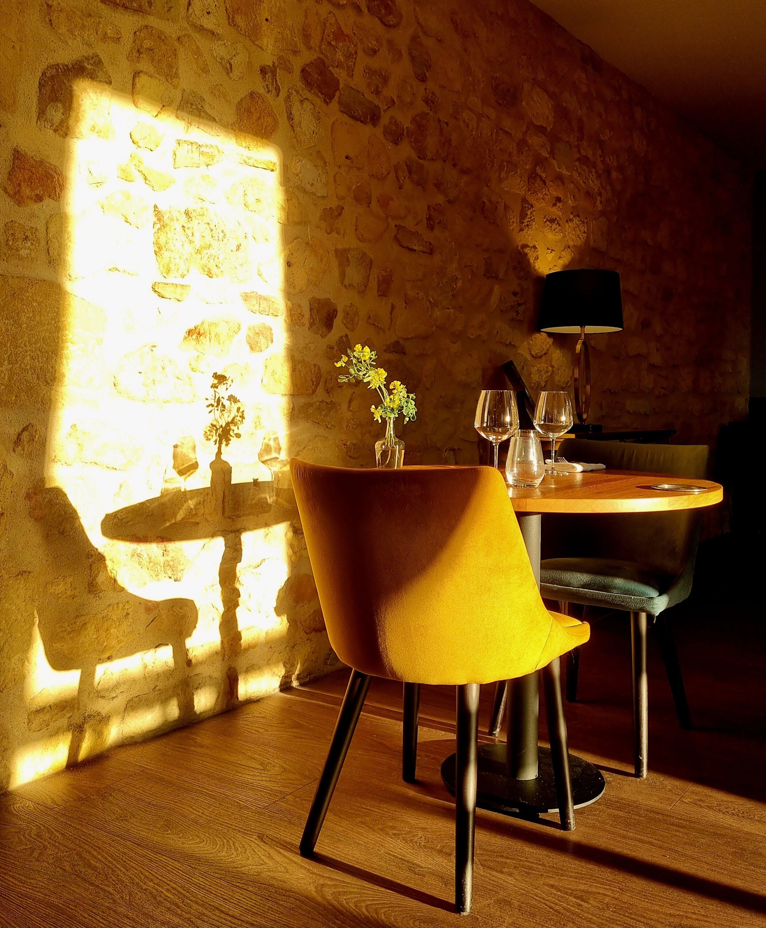 Un comedor con pared de piedra, una mesa con sillas, un jarrón con flores y una lámpara.
