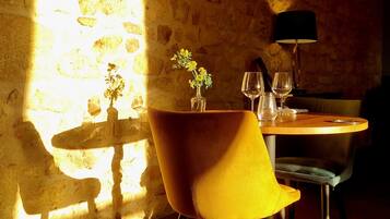 Un comedor con pared de piedra, una mesa con sillas, un jarrón con flores y una lámpara.
