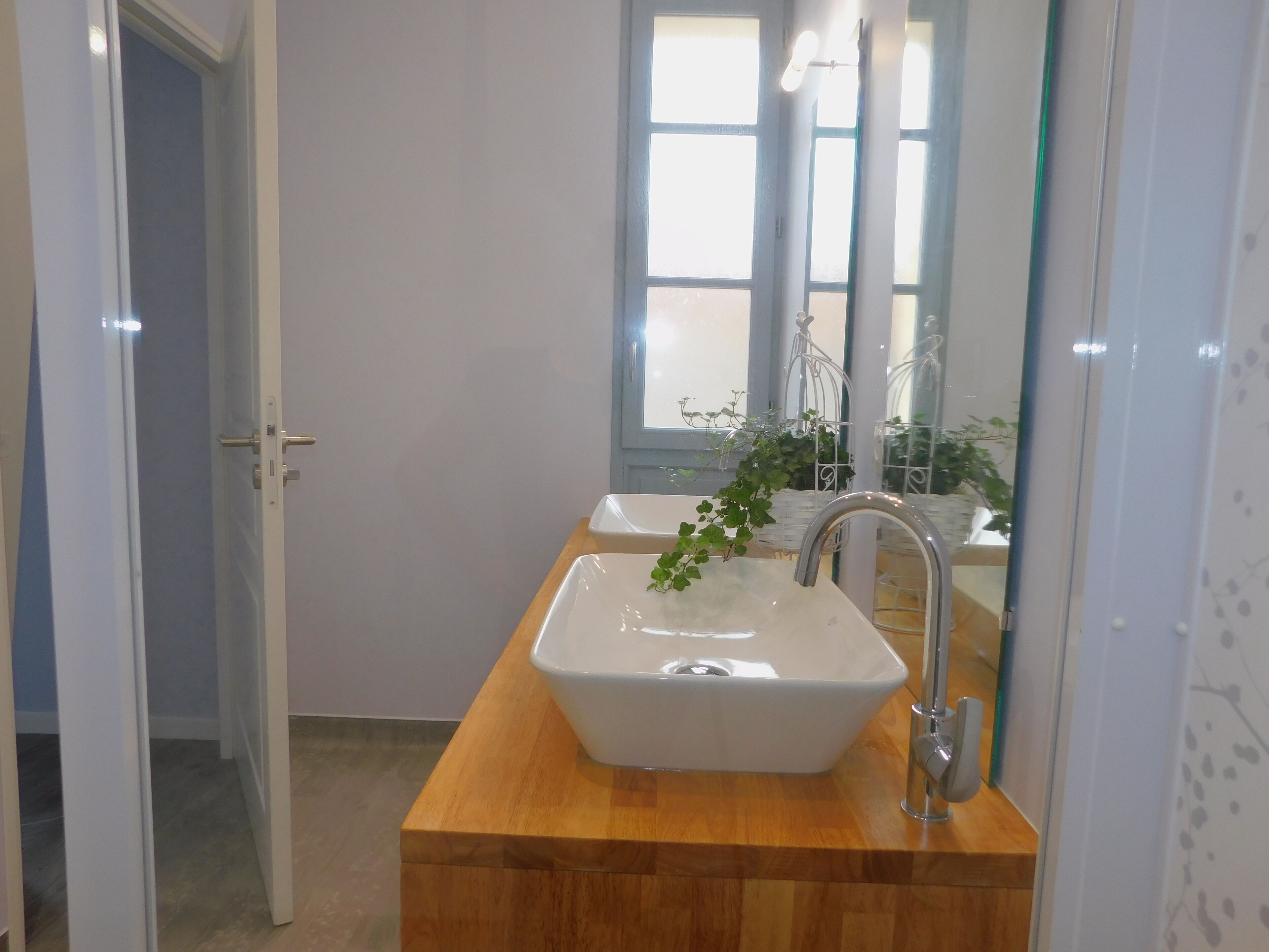 A bathroom with a wooden vanity, two sinks, a mirror, and a window with plants.