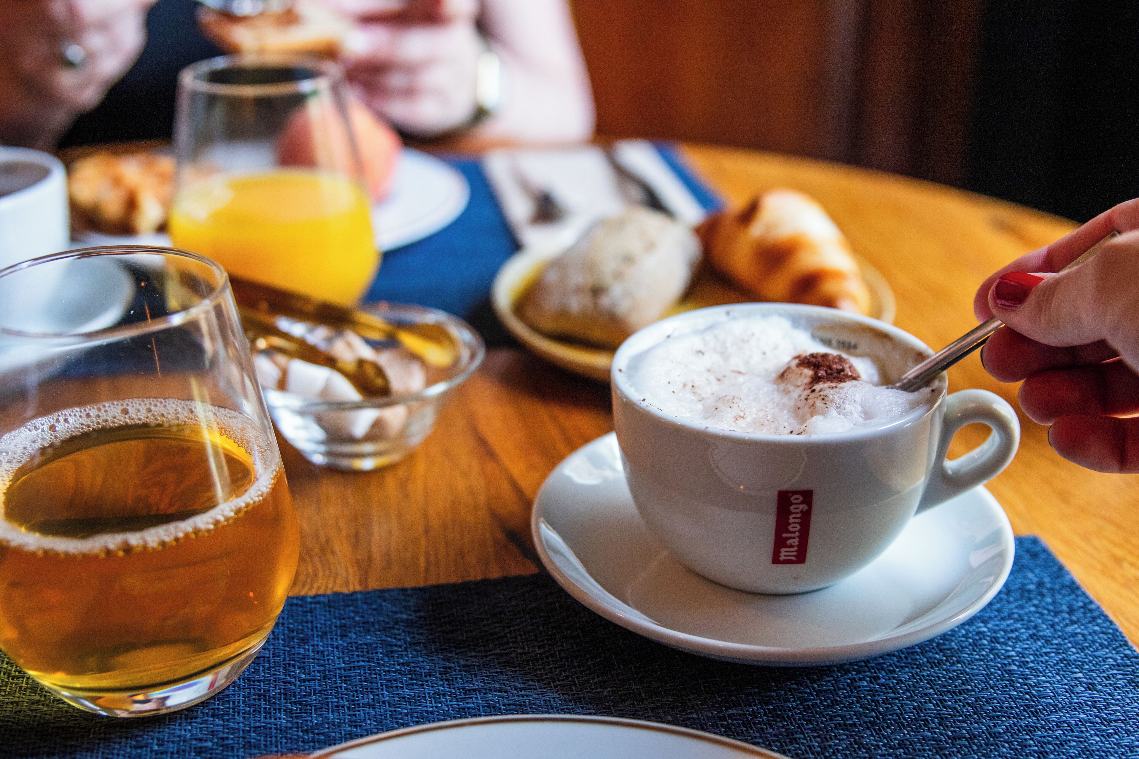 A cup of coffee with a spoon, a glass of beer, and a plate with croissants on a wooden table.