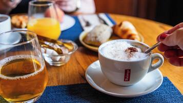 Una taza de café con una cuchara, una jarra de cerveza y un plato con cruasanes sobre una mesa de madera.