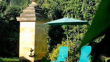 Un jardin agrémenté d’une structure en pierre, d’un parasol vert et de deux chaises bleues.