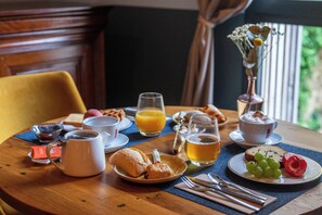 A breakfast table with croissants, a fruit plate, a coffee pot, a glass of orange juice, and a vase with flowers. - Hôtel des Augustins - Boutique Hôtel - Restaurant Gastronomique (Saint-Cyprien)