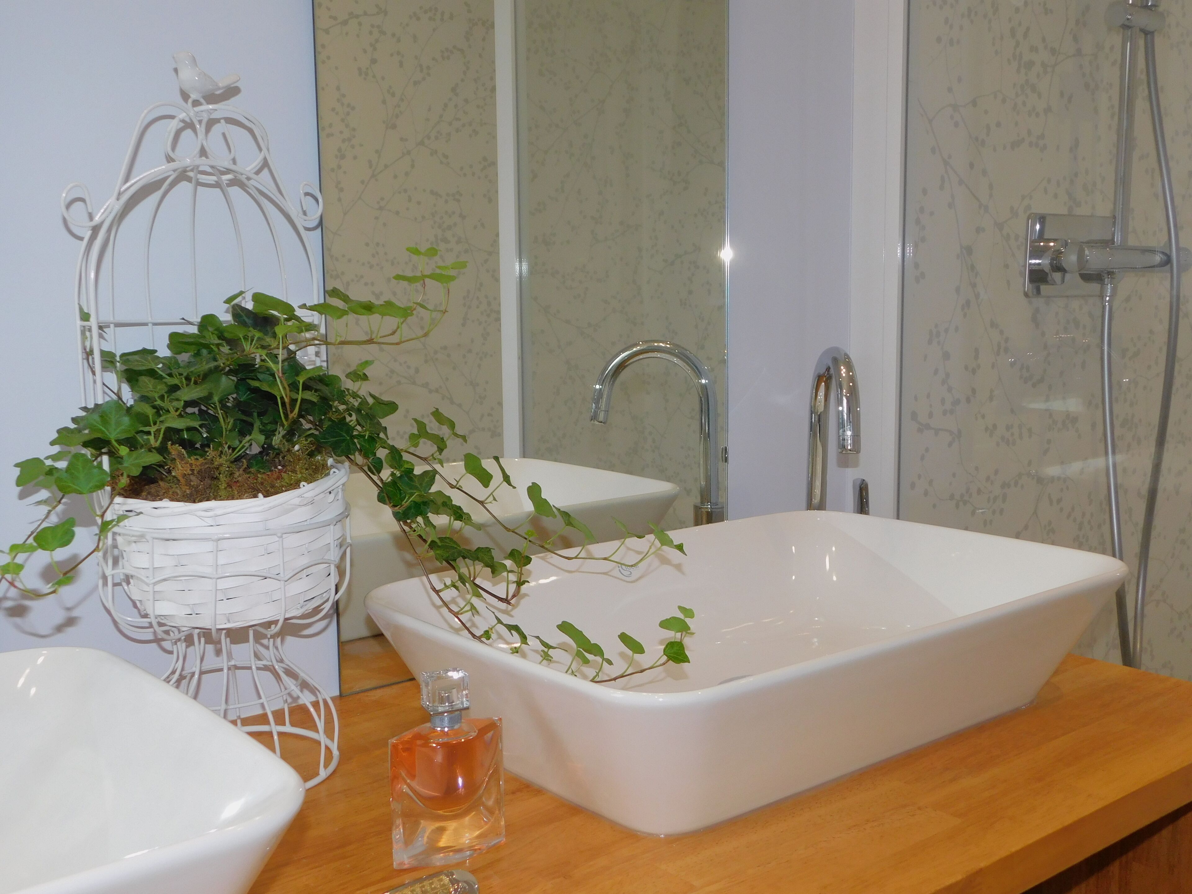 A bathroom with a white sink, a shower, and a decorative birdcage with plants.