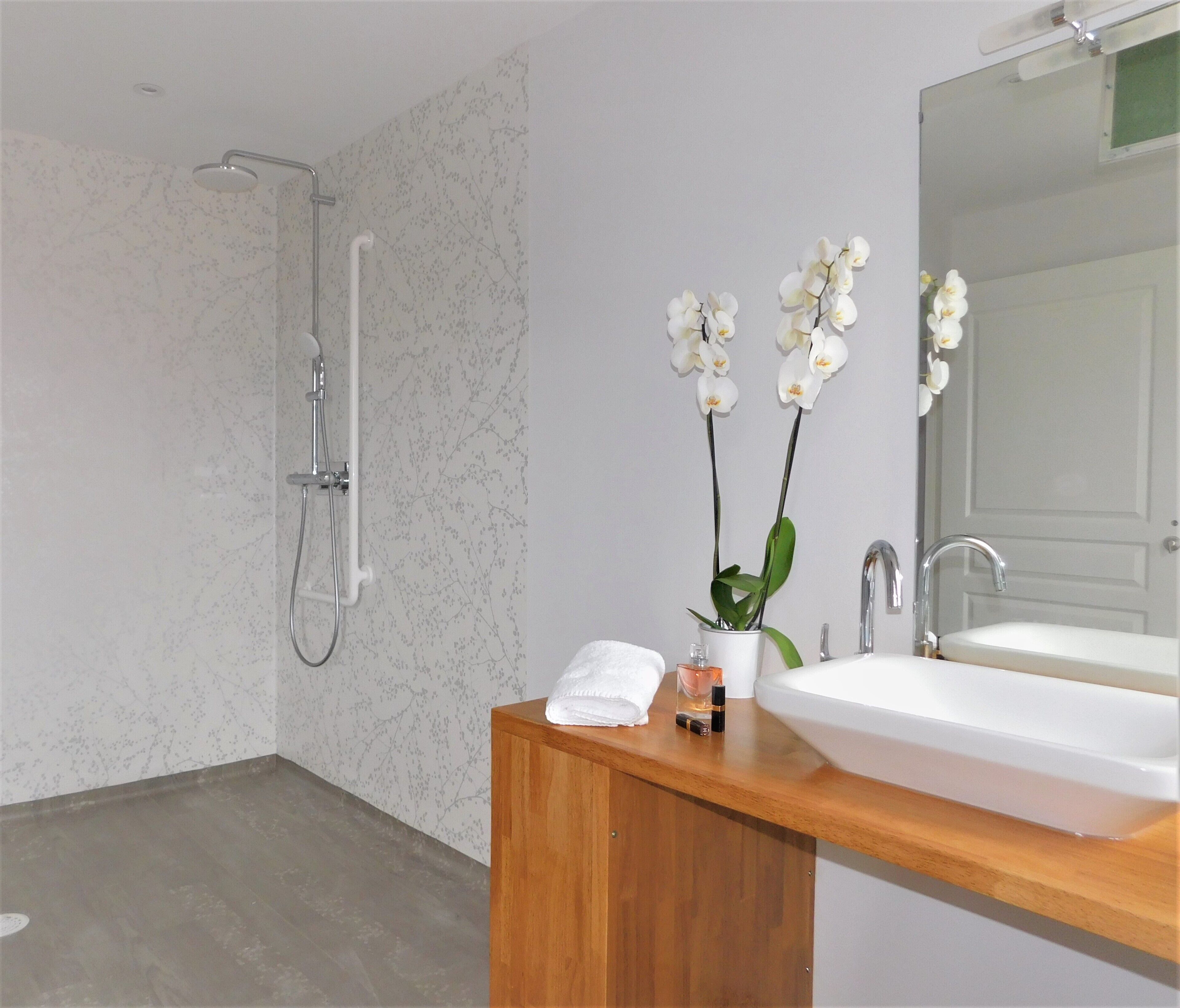 Un baño moderno con ducha, tocador de madera con lavamanos y dos orquídeas blancas.