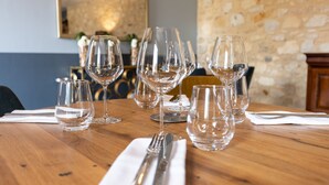A dining table with multiple wine glasses and cutlery, set against a stone wall and a painting. - Hôtel des Augustins - Boutique Hôtel - Restaurant Gastronomique (Saint-Cyprien)