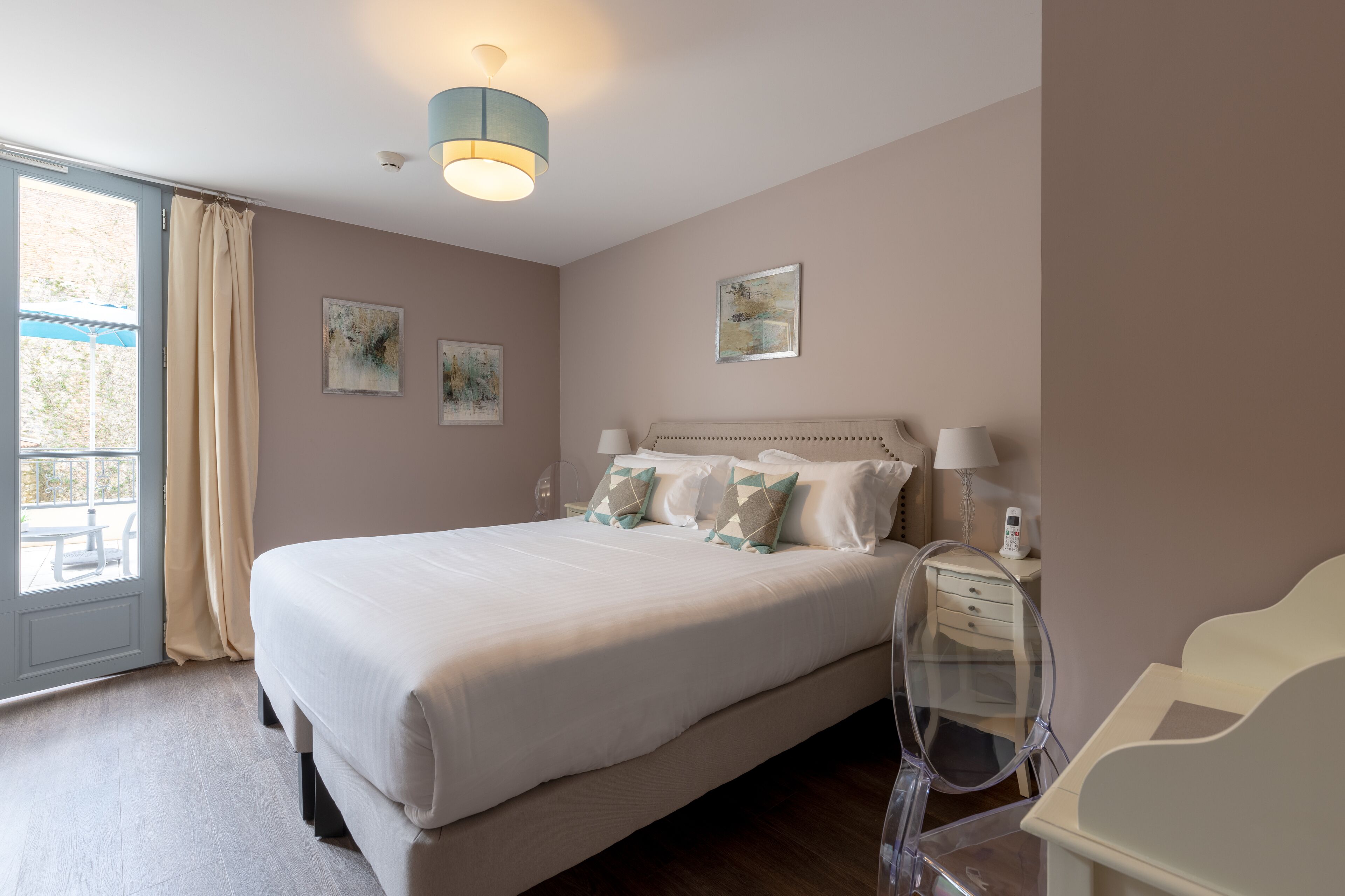A neatly arranged bedroom with a large bed, bedside lamps, and artwork on the walls.