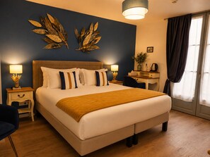 A hotel room with a large bed, two bedside tables, a desk, a chair, a lamp, a plant, and a window with curtains. - Hôtel des Augustins - Boutique Hôtel - Restaurant Gastronomique (Saint-Cyprien)