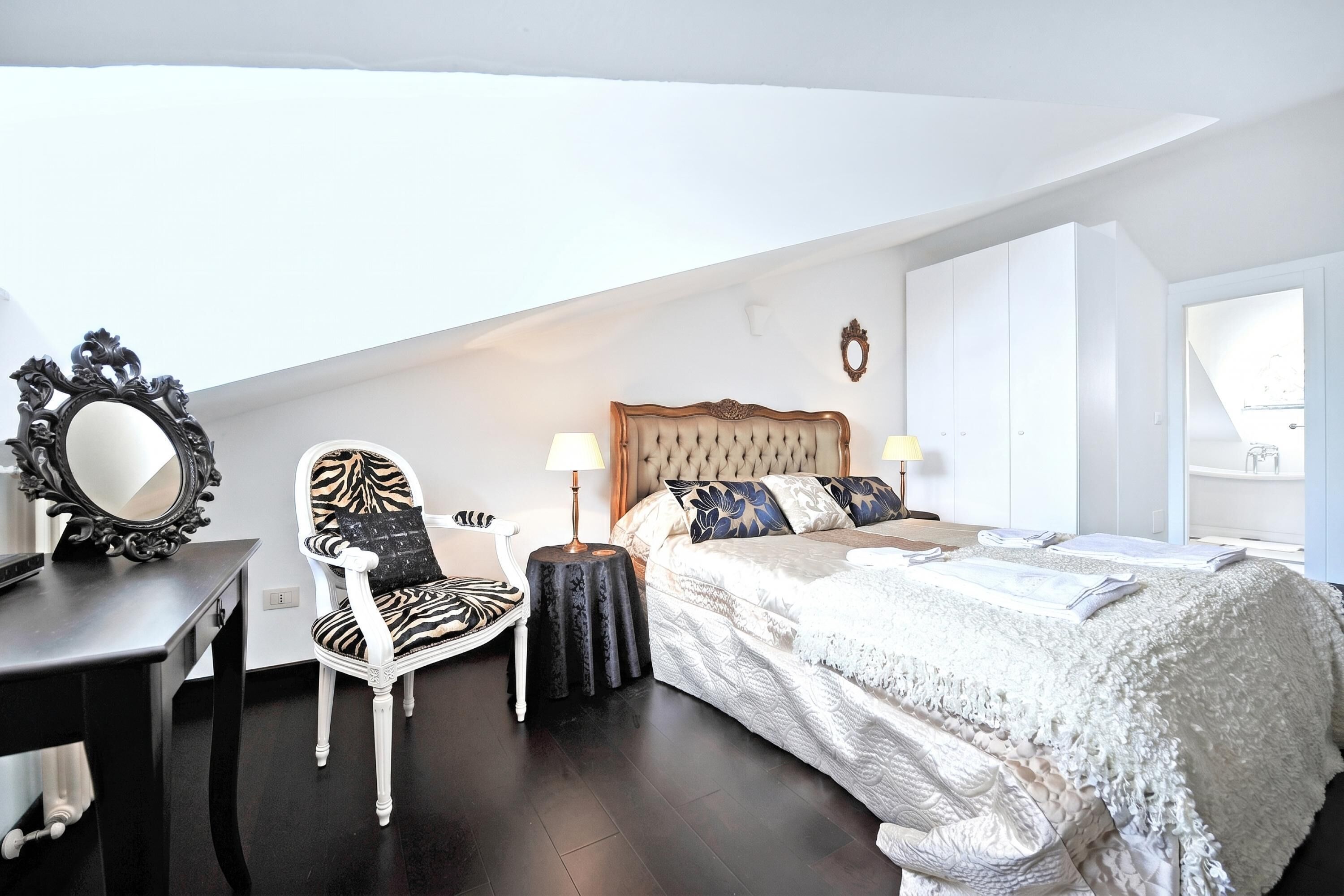 Une chambre à coucher avec un lit, une chaise, un bureau et un miroir.