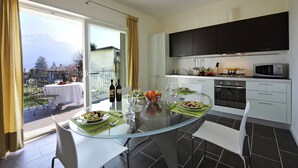 A modern kitchen with dark cabinets, a glass dining table, and a view of the outdoors. - Gravedona Aquamarine Apt. 3 (Gravedona)