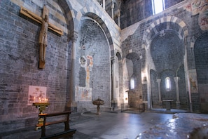 A church interior with stone arches, a wooden crucifix, and a lit candle. - Gravedona Aquamarine Apt. 3 (Gravedona)