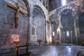 A church interior with stone arches, a wooden crucifix, and a lit candle.