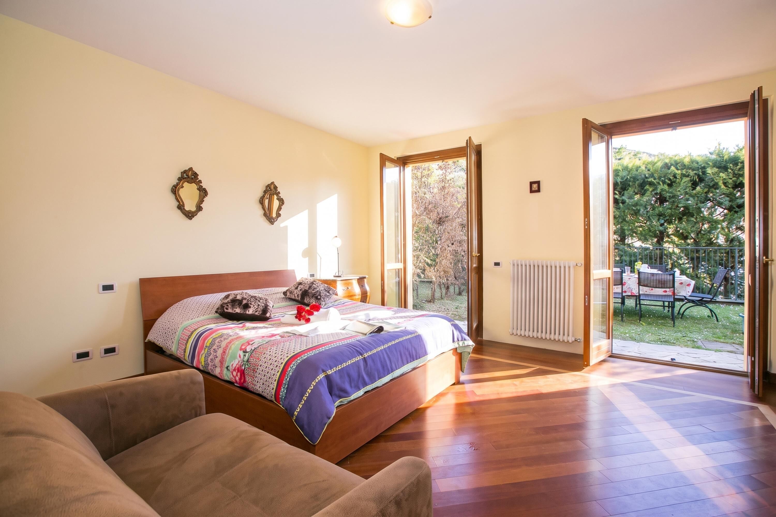 Un dormitorio con una cama grande, un sofá, un radiador y un ventanal corredera que da a un espacio exterior.