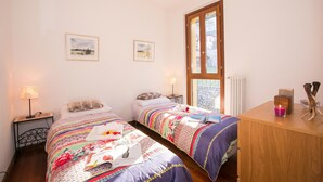 A bedroom with two beds, a wooden desk, a window, and two wall-mounted lamps. - Regina Villetta (Laglio)
