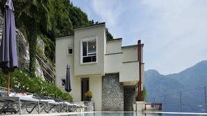 A modern building with a pool, lounge chairs, and a mountain backdrop. - Villa Parisi (Tremezzina)