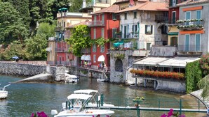A waterfront area with boats docked, a stone bridge, and buildings with balconies and flower boxes. - Villa Parisi (Tremezzina)