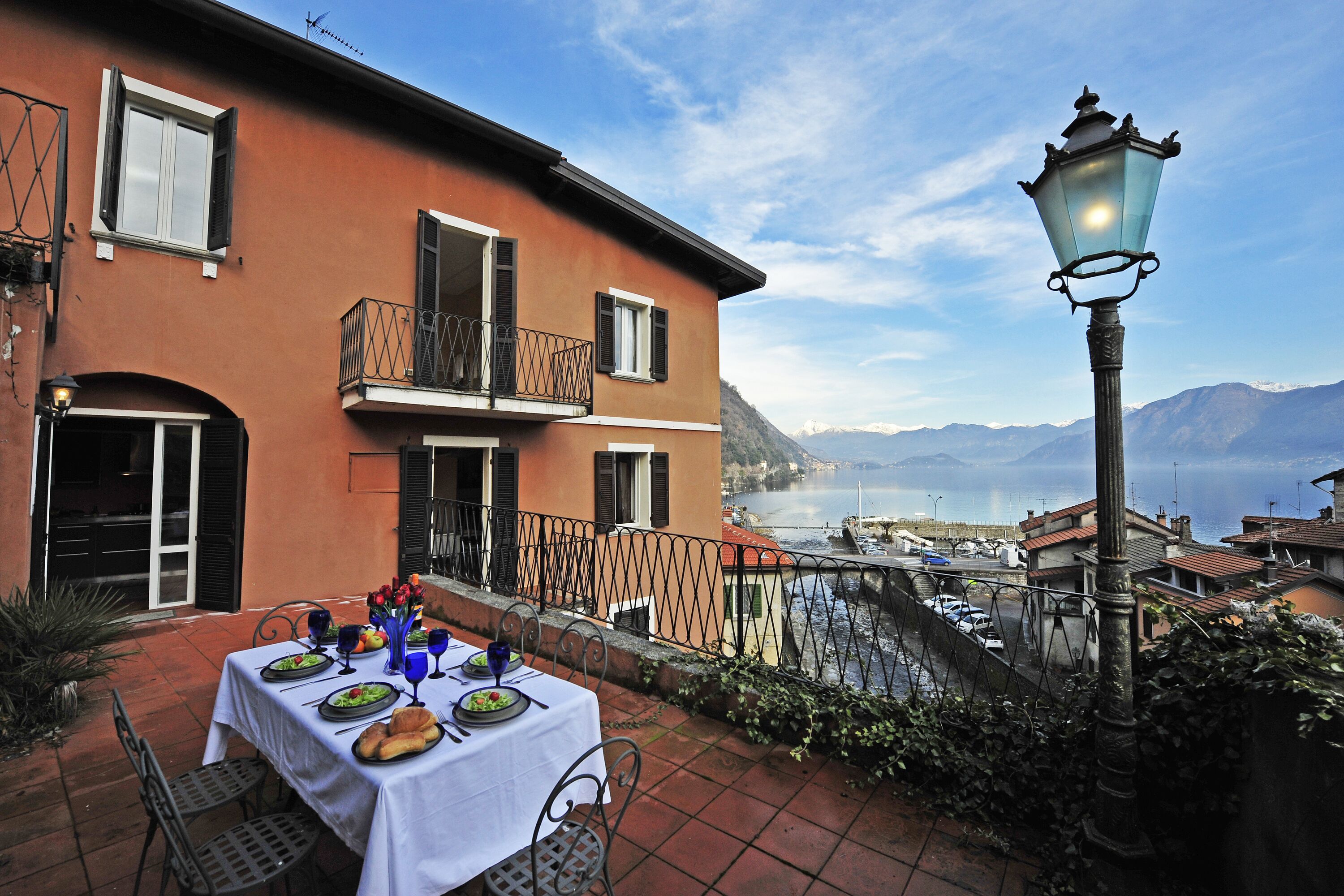 A dining area with a table set for two, overlooking a scenic waterfront with boats and mountains in the background.