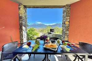 A table set for breakfast with a mountain view, stone walls, and outdoor seating.