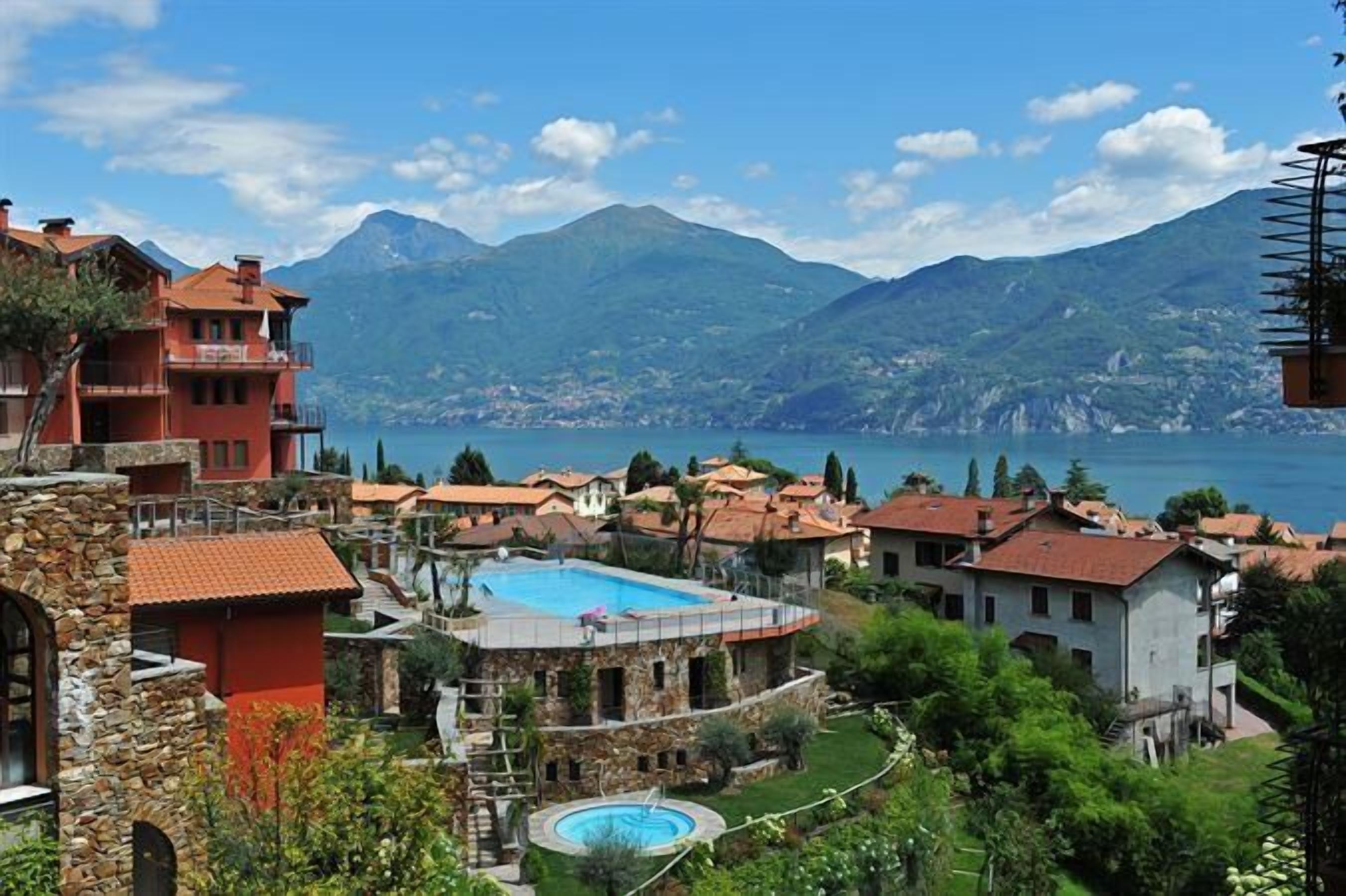 Un complexe hôtelier doté d’une piscine, de bâtiments en pierre et offrant une vue sur les montagnes et un lac.