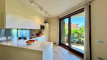 Une cuisine moderne dotée d’un grand îlot central, d’appareils électroménagers intégrés et donnant sur un balcon.