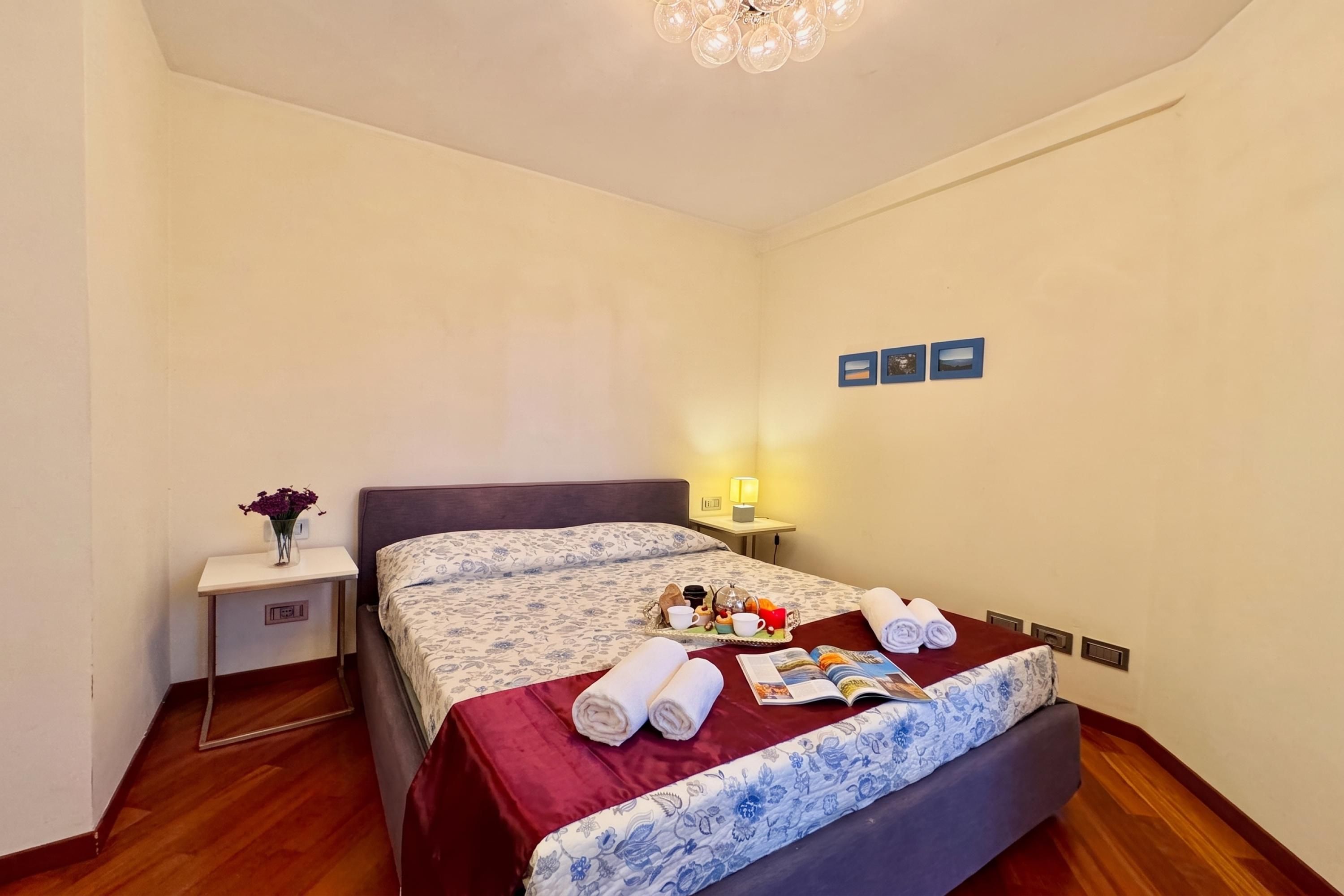 A hotel room with a bed, bedside table, lamp, and wall art.