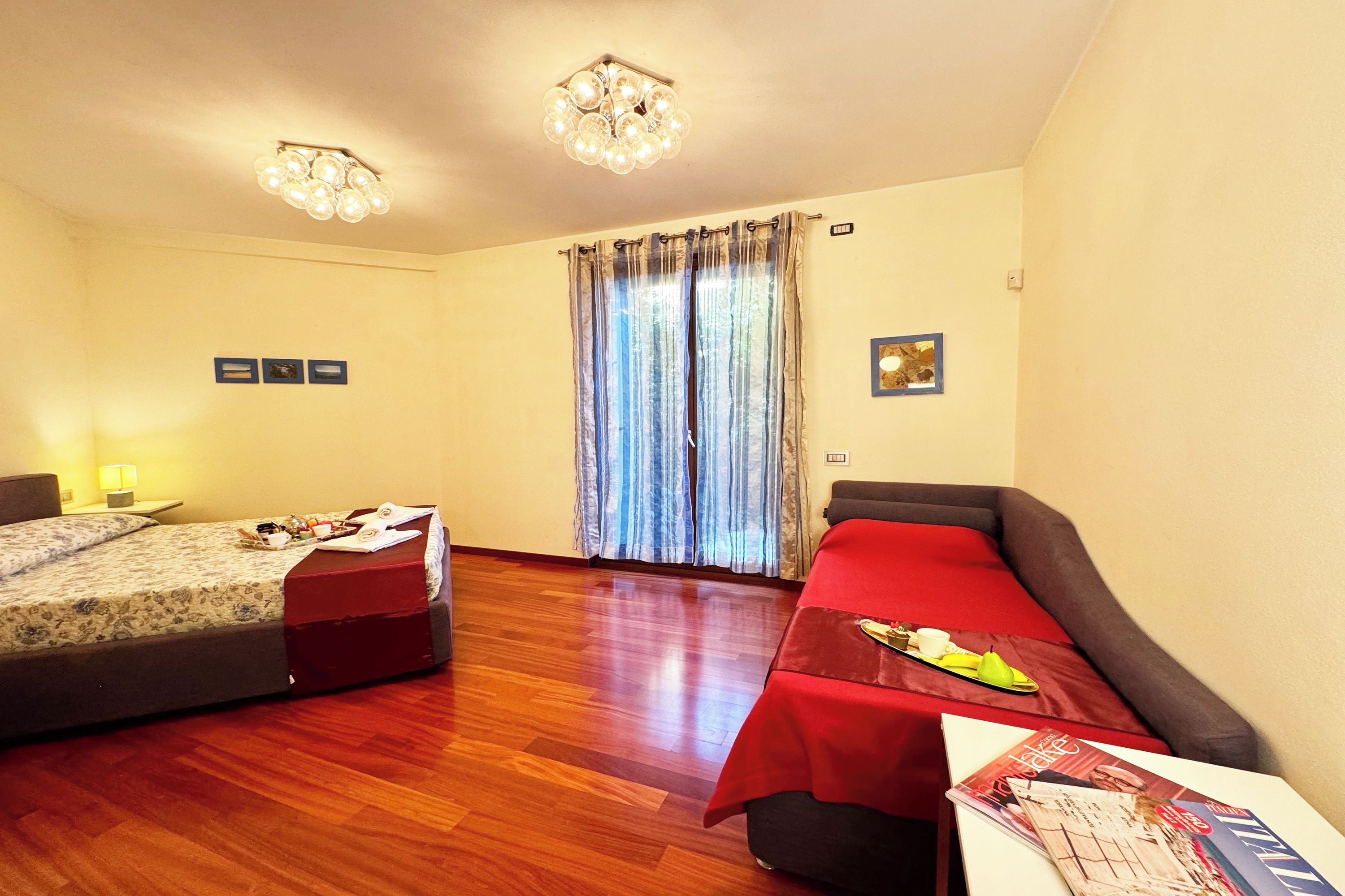 A hotel room with two beds, wooden flooring, a chandelier, curtains, and a magazine on the table.