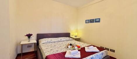 A neatly arranged hotel room with a bed, bedside table, and a small table with a vase of flowers.
