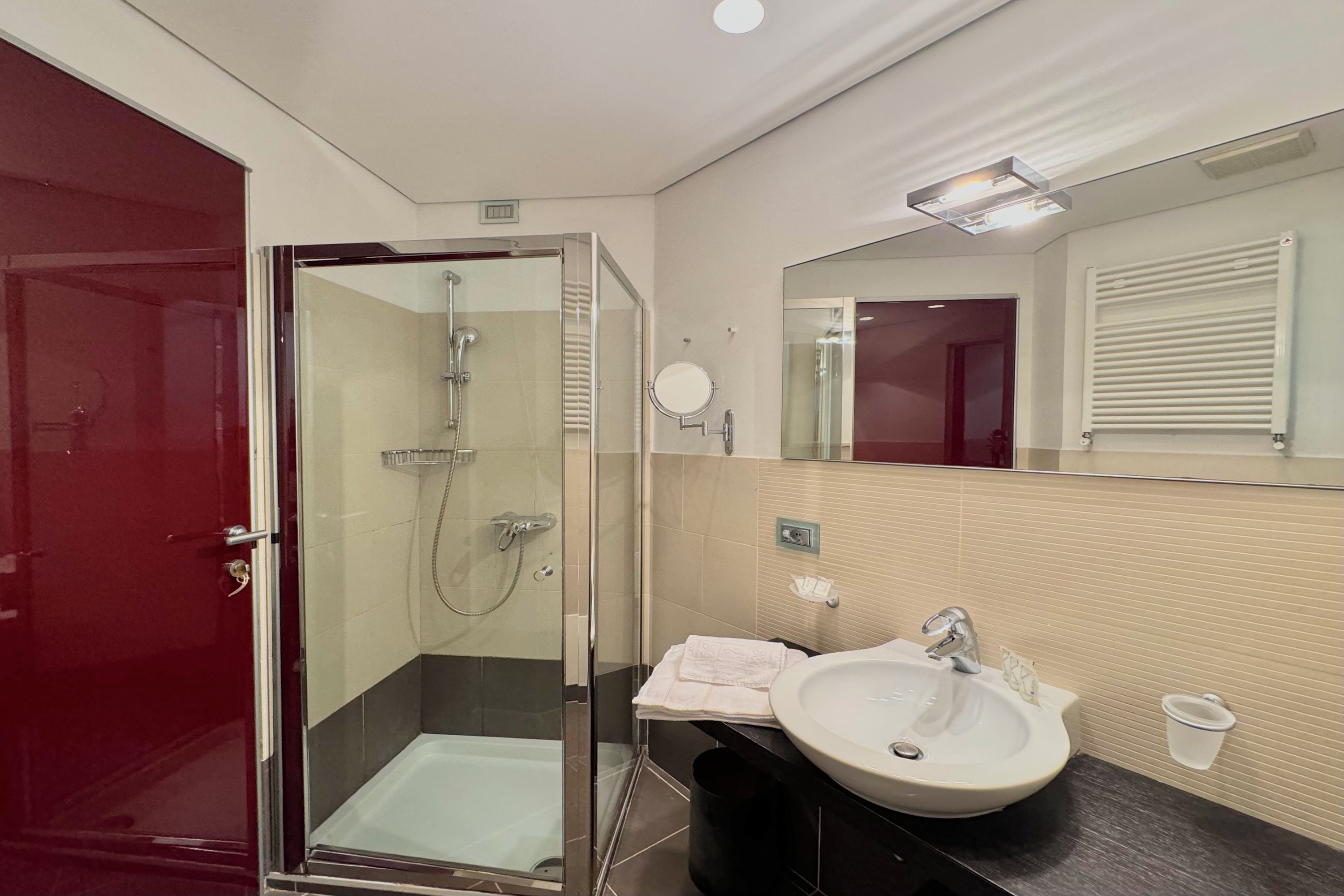 A modern bathroom with a glass-enclosed shower, a sink with a mirror, and a red door.