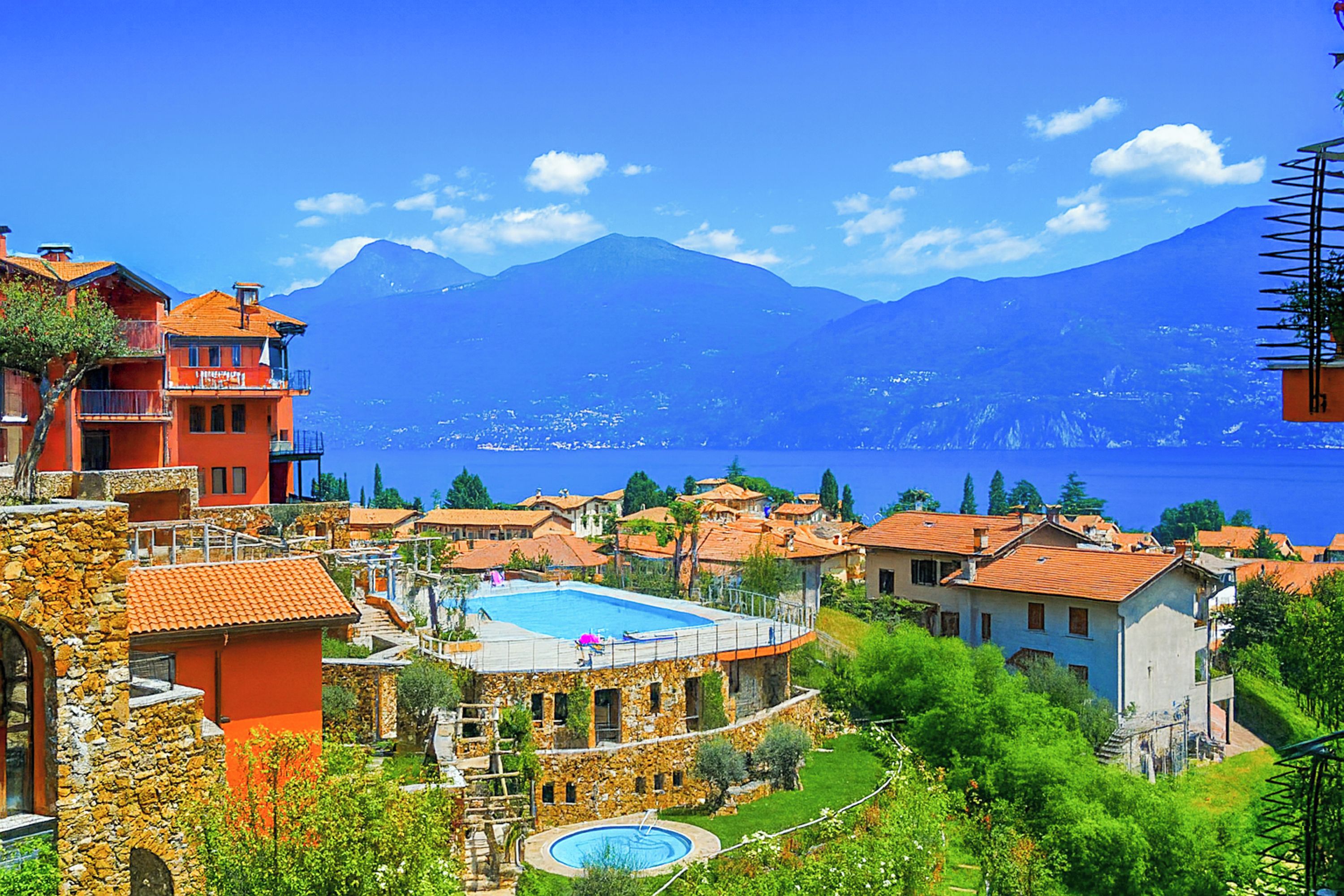 A coastal village with traditional architecture, a swimming pool, and a view of the sea and mountains.