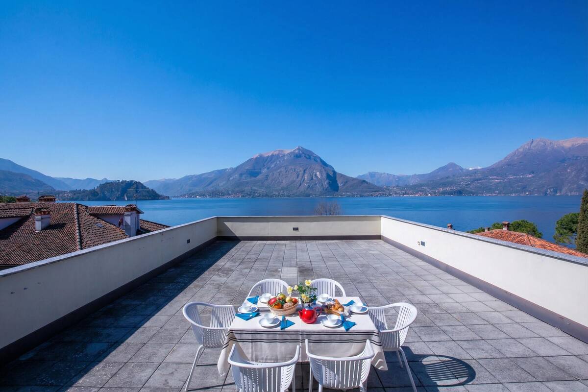 Une terrasse avec une table dressée pour le dîner, offrant une vue sur un lac et des montagnes.