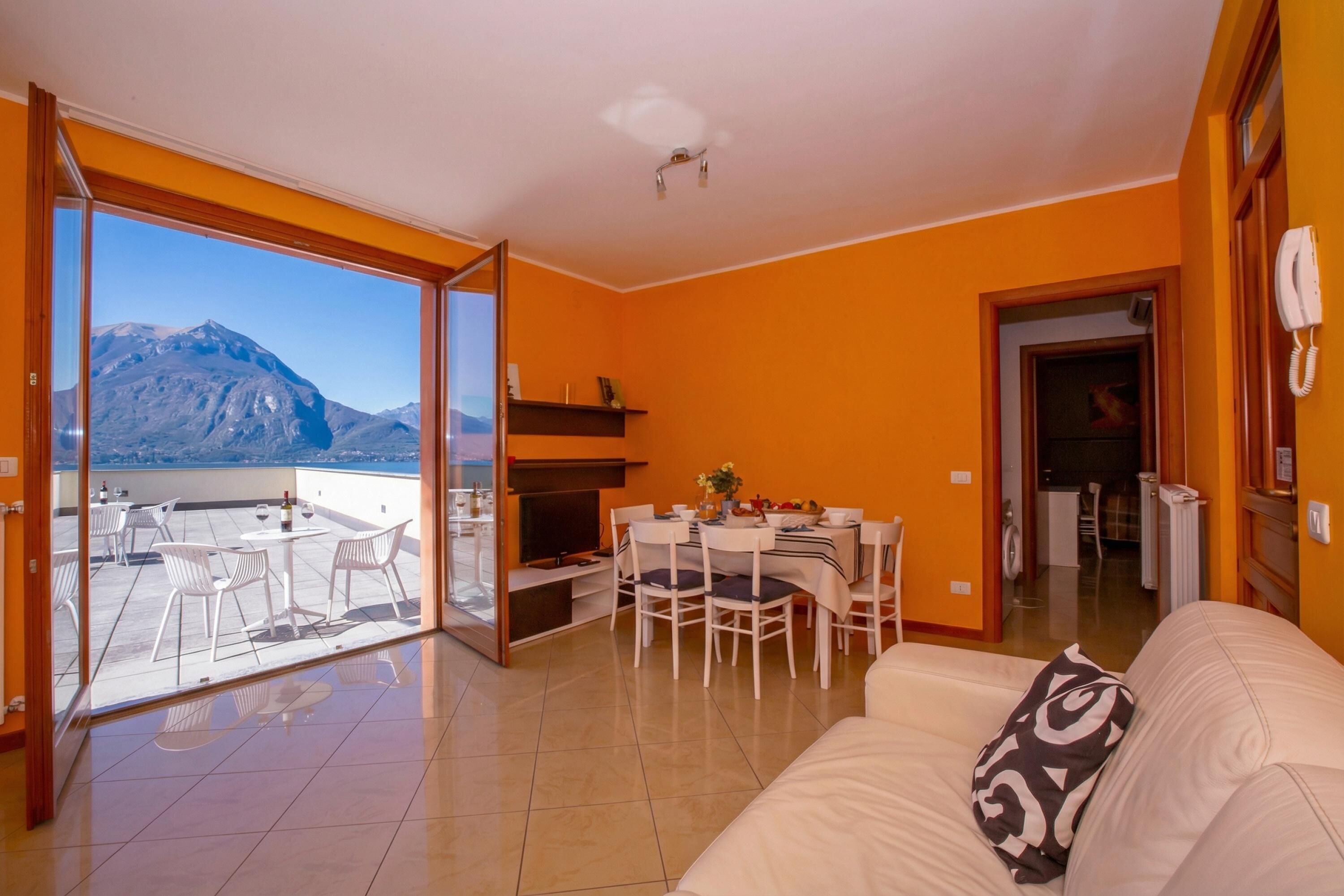 Una sala de estar con un sofá, una mesa de comedor con sillas, un televisor y vistas a montañas a través de un ventanal.