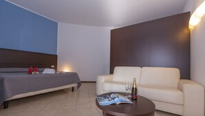 A hotel room with a bed, a sofa, a small table with a magazine and a bottle, and a wall-mounted light. - Fontana Del Lago Apt. 8 (Varenna)