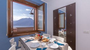 A dining area with a table set for two, a window with a mountain view, and a mirror reflecting the room. - Fontana Del Lago Apt. 8 (Varenna)