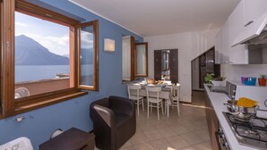 A compact kitchen with a dining area, a large window with a view of mountains, and a view of the sea. - Fontana Del Lago Apt. 8 (Varenna)