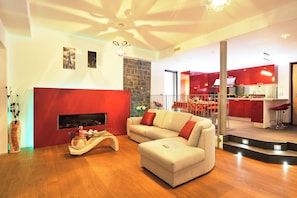 A modern living room with a fireplace, a sofa, and a kitchen in the background.