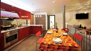 A modern kitchen with red cabinets, a dining table set with plates and cutlery, and a TV mounted on the wall. - Villa Bianca - Grande (Menaggio)