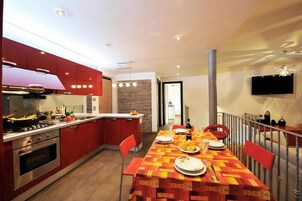 Una cocina moderna con armarios rojos, una mesa de comedor dispuesta con platos y cubiertos, y un televisor montado en la pared.