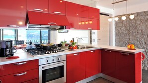 A modern kitchen with red cabinets, stainless steel appliances, and a stone accent wall. - Villa Bianca - Grande (Menaggio)