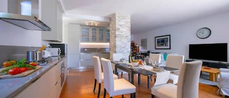 A modern kitchen with white cabinets, a stone pillar, and a dining area with white chairs and a table set for four.