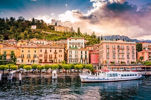 Un hotel frente al agua con un muelle para barcos, edificios con balcones y montañas al fondo.