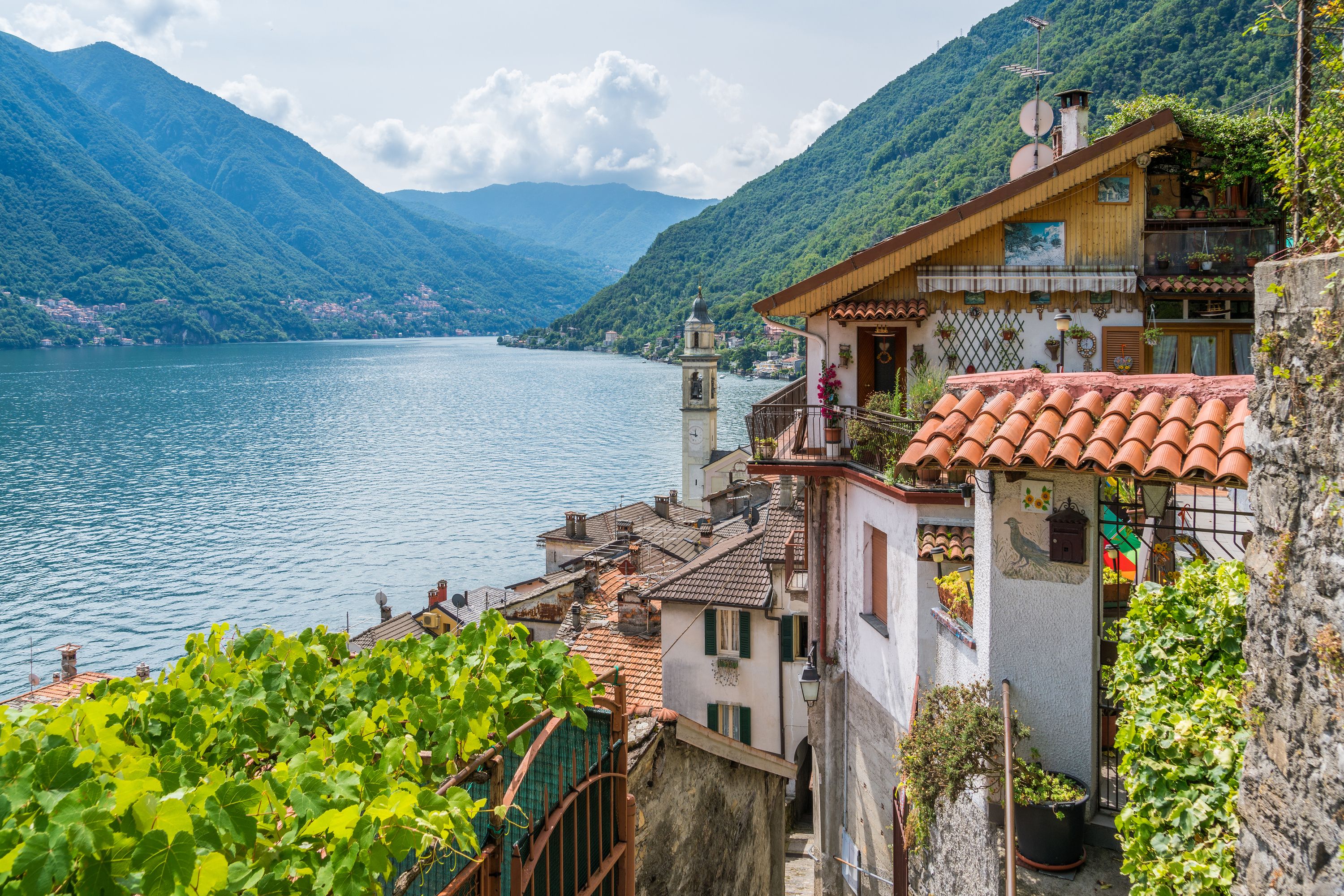 A coastal building with a bell tower, terracotta roof tiles, and a view of a lake and mountains.